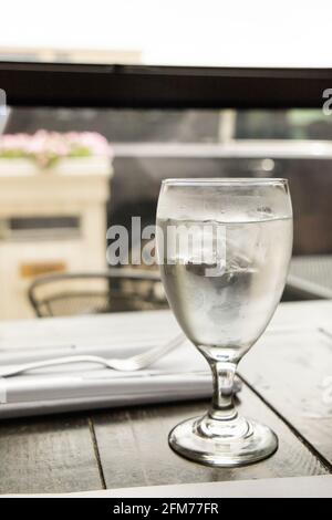 A water glass and a silverware setting on a wood table at a high end restaurant Stock Photo