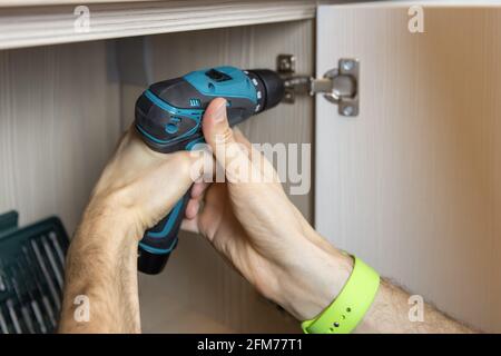 An unrecognizable man installs a door on a wardrobe, fixes furniture with a screwdriver. Only hands are visible. Close-up. Renovation concept, furnitu Stock Photo