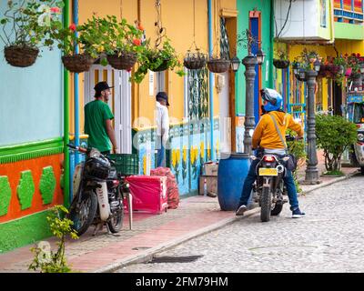 Guatape, Antioquia  Colombia - April 3 2021: A Man on a Motorcycle is Talking to Another Man on the Street of the Colorful Village Stock Photo