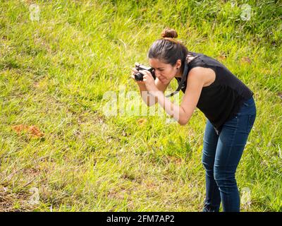 Young Short Hispanic Woman in Blue Jeans and Black Shirt Takes Picture with Compact Mirrorless Camera Stock Photo