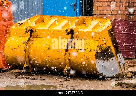 Industrial excavator or bulldozer old worn out broken damaged bucket at construction site background in cold winter snowfall. Stock Photo
