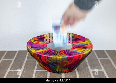 A human hand drops a swiss banknote into a basket dressed in colorful fabric Stock Photo