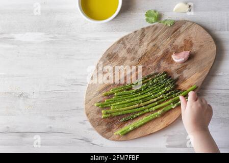 Top view of a woman's hand arranging green asparaguses on a wooden board in the kitchen Stock Photo