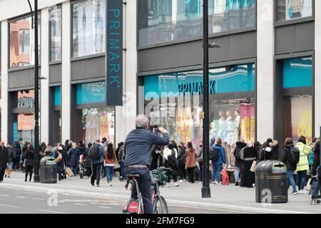 A man on a bicycle takes a photo of the queue outside a Primark store on the first day non-essential stores reopened as part of lockdown easing Stock Photo