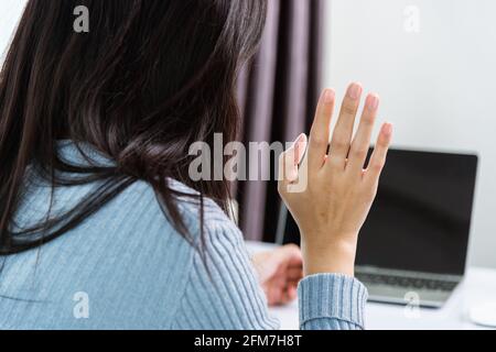Work from home, Back of Asian young businesswoman video conference call or facetime meeting online raise hand to to say hello on front laptop computer Stock Photo