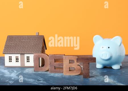 Word DEBT with model of house and piggy bank on color background Stock Photo
