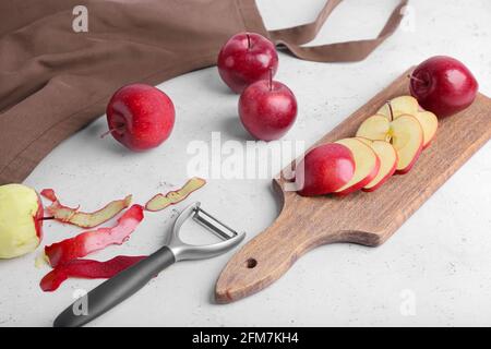Board with cut red apples and peeler on table Stock Photo