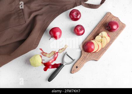 Board with cut red apples and peeler on table Stock Photo