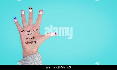 A hand with finger faces wearing face masks and keeping apart, mask up and keep apart text on hand, with copy space, wearing a mask and social distanc Stock Photo
