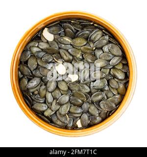 top view of crude styrian pumpkin seeds in round ceramic bowl cutout on white background Stock Photo