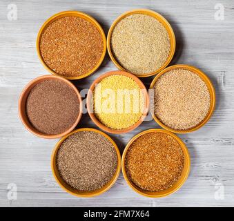 top view of various millet grains in round ceramic bowls on gray wooden table Stock Photo