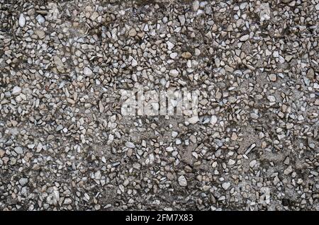 Background formed by the lower part of the facade of the building, a fragment of the wall with inclusions of gray stone pebbles in black asphalt and d Stock Photo