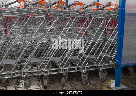 Row of metal shopping carts with orange handles standing tightly one in another outdoor in front of DIY store in specially designated place on rainy c Stock Photo