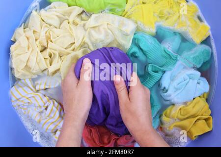 Female hands wash colored clothes in basin. Top view. Stock Photo