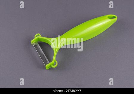 Green Vegetable peeler on gray background. Hand-held tool for removing peels. Stock Photo