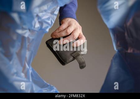 A hand tosses an old black wallet into a trash can. Man holds empty leather purse over garbage basket. View from below. Indoors. Stock Photo