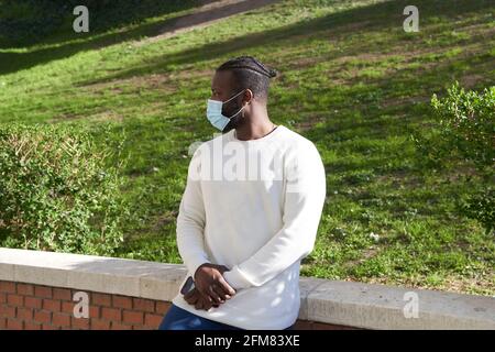 Young African American man leaning against a wall wearing an anti-contagion mask. Latino man walking around the city with face mask. Concept of new normality. High quality photo Stock Photo