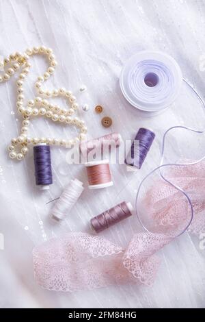 Items for tailoring - spools of thread, needles, ribbons, lace, buttons, pearl necklace on a background of tulle with sequins. Stock Photo