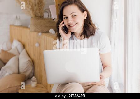 Smiling young Caucasian woman record digital audio message on smartphone in modern flat Stock Photo