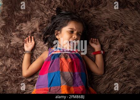 Sleeping kid, a girl child showing different gestaurs who is lying on a synthatic rug which is very soft and brown in colour Stock Photo