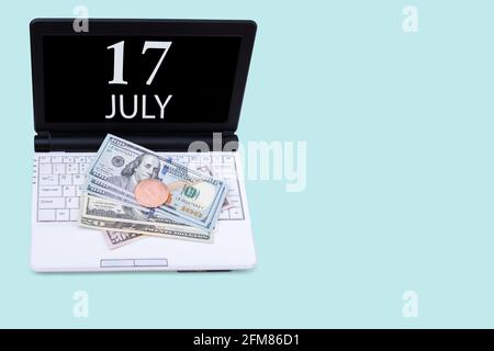 17th day of july. Laptop with the date of 17 july and cryptocurrency Bitcoin, dollars on a blue background. Buy or sell cryptocurrency. Stock market c Stock Photo