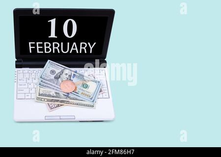 10th day of february. Laptop with the date of 10 february and cryptocurrency Bitcoin, dollars on a blue background. Buy or sell cryptocurrency. Stock Stock Photo