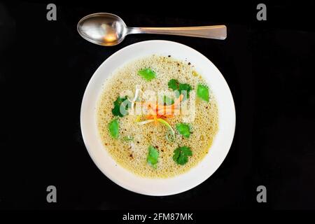 Whipped strong asparagus puree soup with herb and vegetable julienne in white plate on black background. Stock Photo