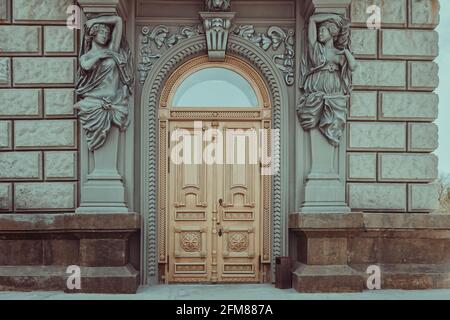 Large carved wooden door. Nice entrance with wooden door and statues. Entrance to a gray building Stock Photo