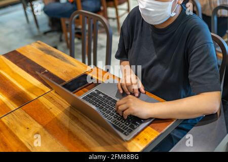 Woman wearing protective mask and using laptop at cafeteria  Stock Photo