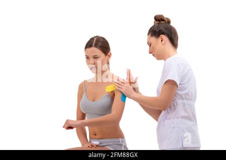 Physiotherapist putting on kinesio tape on female patients shoulder isolated on white background. rehabilitation concept Stock Photo