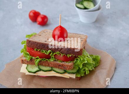 Delicious sandwich with fresh lettuce leaves, tomatoes, cucumbers and cheese on a grey table background. Stock Photo