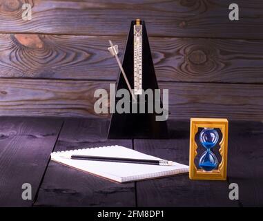 hourglass, metronome and memo pad with a pencil on a wooden table Stock Photo