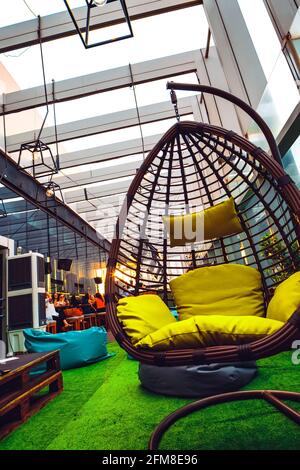 Wicker hammock chair with yellow pillows on the terrace, against the background of artificial green grass Stock Photo