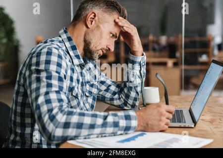 Brooding grey man working with laptop while sitting in office Stock Photo