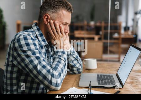Tired grey man working with laptop while sitting in office Stock Photo