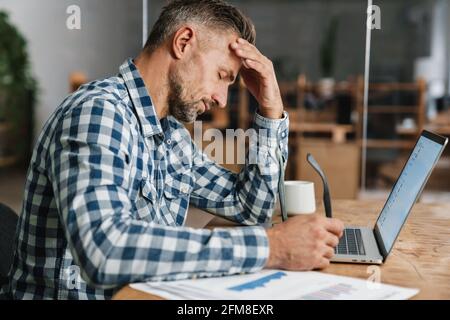 Tired grey man working with laptop while sitting in office Stock Photo