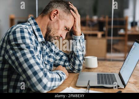 Tired grey man working with laptop while sitting in office Stock Photo