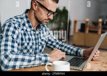 Focused unshaven man in eyeglasses working with laptop in office Stock Photo