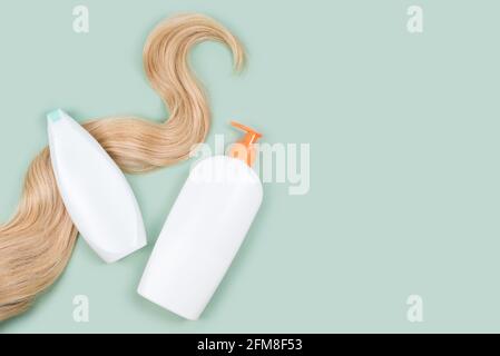 Shampoo wrapped in lock of curly blonde hair and conditioner bottle mockups on mint background, top view. Flat lay in pastel colors. Hair care Stock Photo