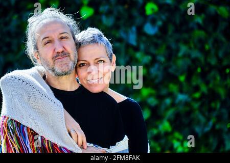 Mature and happy caucasian couple posing hugging outdoor in a garden with a leaves background. Stock Photo