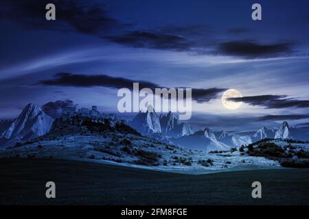 castle on the hill at night. composite fantasy landscape. grassy meadow in the foreground. rocky peaks of the ridge in the distant background in full Stock Photo