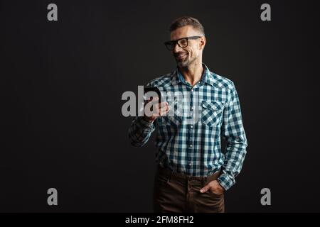 Image of a smiling optimistic grey-haired man using mobile phone isolated over grey wall background Stock Photo