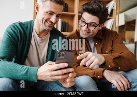 Happy young gay couple using mobile phone while sitting on a sofa in the living room Stock Photo