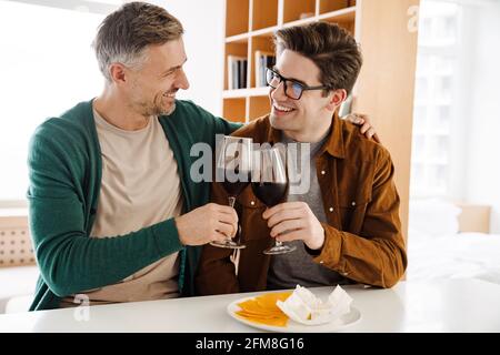 Happy caucasian gay couple hugging while drinking wine at home Stock Photo