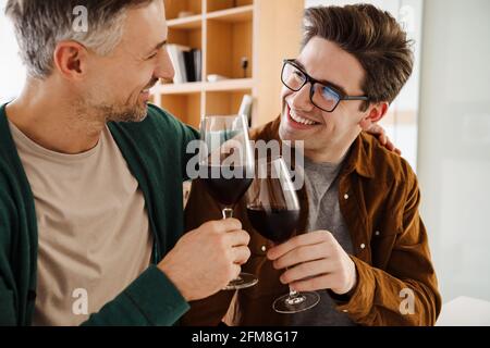 Happy caucasian gay couple hugging while drinking wine at home Stock Photo