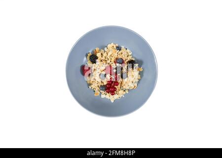 Top view of appetizing oatmeal with fresh berries and nuts in beautiful blue plate on white background. Concept of tasty porridge to support the figure or for emaciation.  Stock Photo