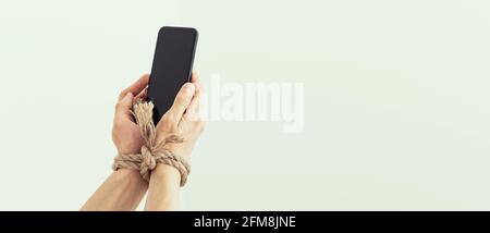 Hands tied with rope on a white background, suggesting internet addiction or social media addiction Stock Photo