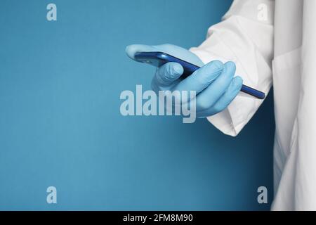 doctor's hand in protective gloves using a smartphone against blue background  Stock Photo