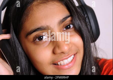 Girl in the headphones lovely indian girl teenager 14 years old listens to music on headphones, relaxes, enjoys music lover since childhood Stock Photo