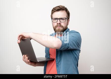 Serious, concentrated bearded man with glasses holds a laptop in hands and looks sternly at the camera. White background. Stock Photo